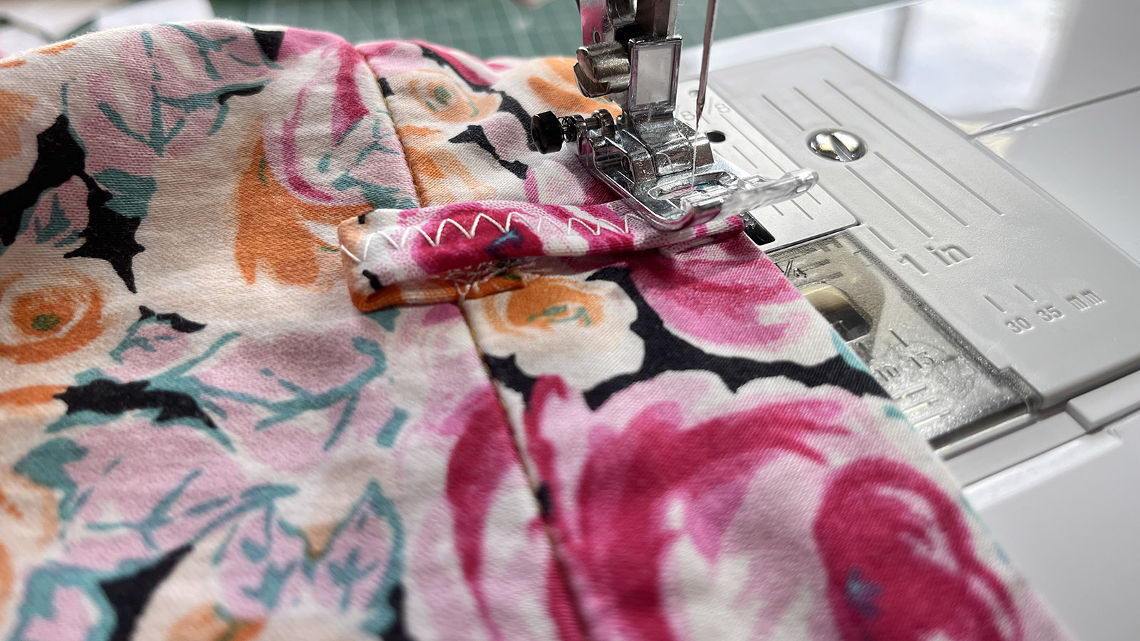 Close up photo of sewing a belt loop to a waistband of floral trousers.